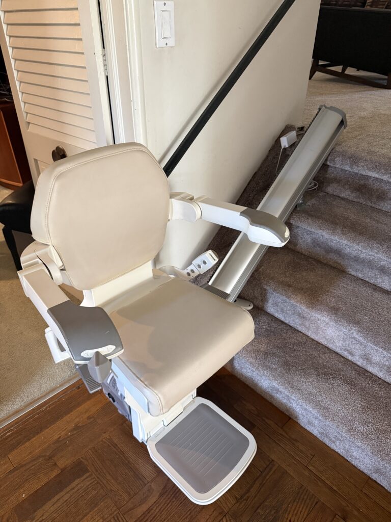 Beige stair lift installed along a carpeted staircase in Plainview
